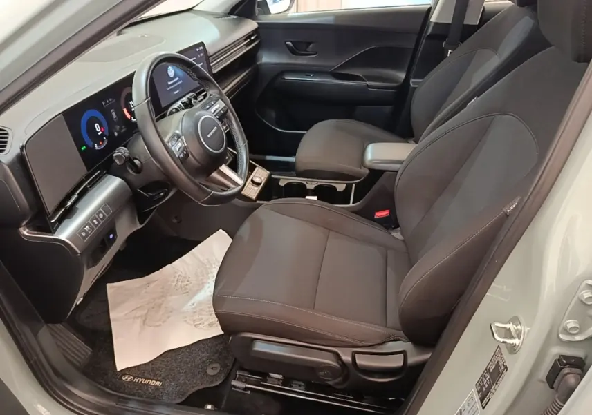 Vue intérieure côté conducteur du Hyundai Kona 2024, sièges noirs et tableau de bord avec écran tactile large.