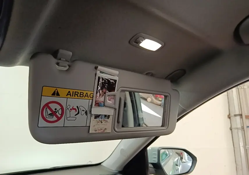 Détail intérieur du pare-soleil côté conducteur avec miroir et autocollants dans un Hyundai Kona vert 2024.