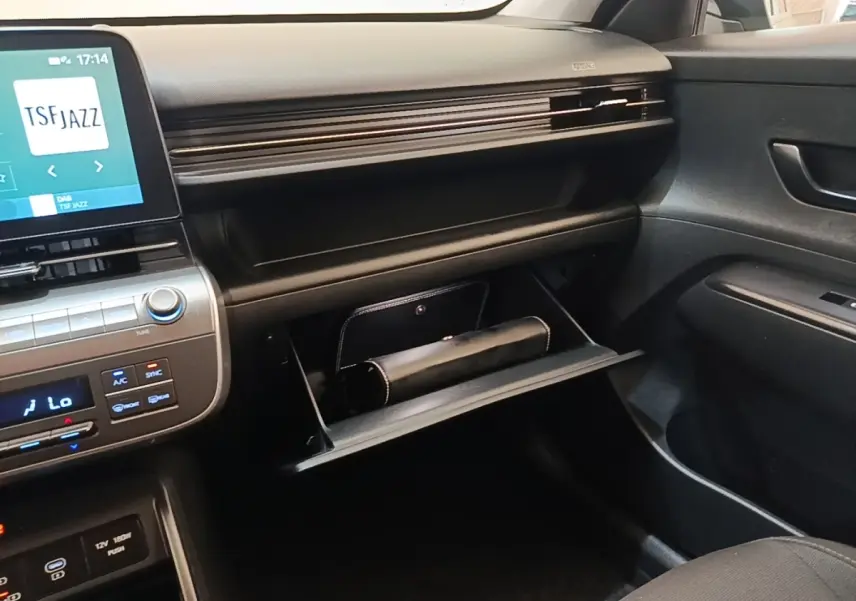 Intérieur de la Hyundai Kona 1.6 Hybrid 2024, vue côté passager sur la boîte à gants ouverte et tableau de bord noir.