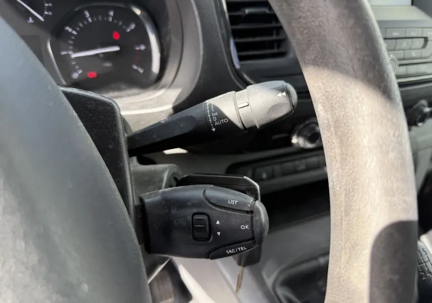 Gros plan sur les commandes au volant noir du Peugeot Expert FGN blanc de 2017, avec tableau de bord partiellement visible.