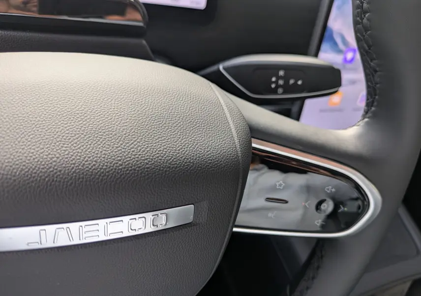 Gros plan sur le volant noir du JAECOO J7 avec logo métallique et commandes tactiles intégrées.