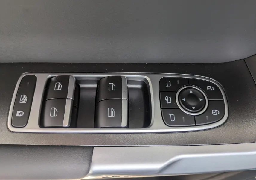 Vue rapprochée des commandes de lève-vitres et réglages des rétroviseurs sur la porte côté conducteur du JAECOO J7 olive gris métal.