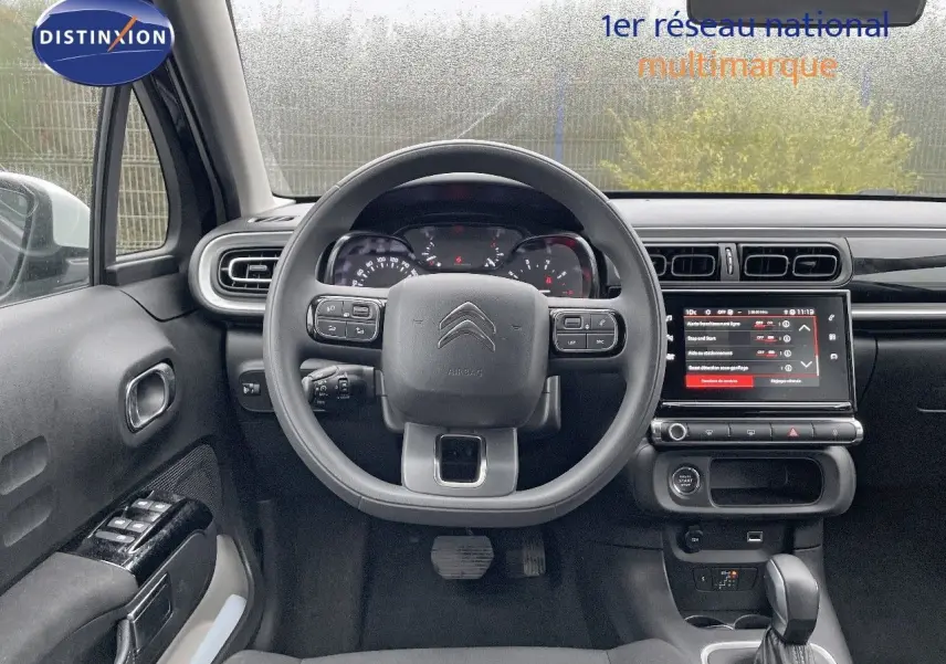 Vue intérieure centrée sur le volant et le tableau de bord d'une Citroën C3 noire métal 2023 avec écran tactile allumé.