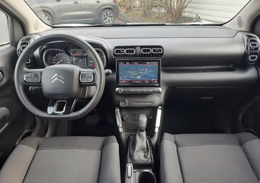 Vue intérieure frontale du tableau de bord et volant noir du Citroën C3 Aircross blanc banquise 2024 avec écran tactile central et boîte auto.