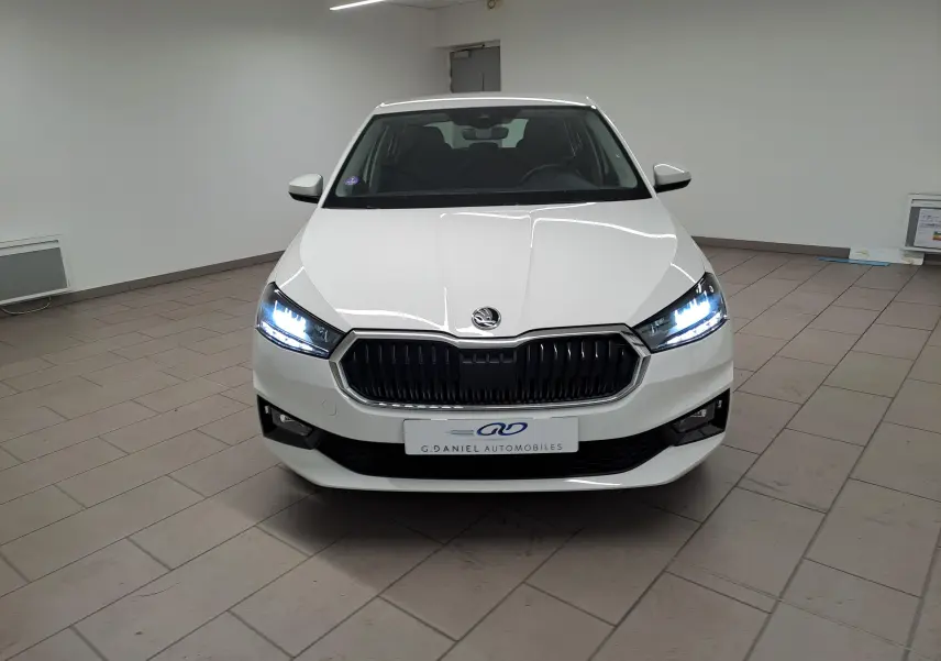 Vue frontale d'une Skoda Fabia 2023 blanc candy avec phares allumés et calandre noire dans un showroom.