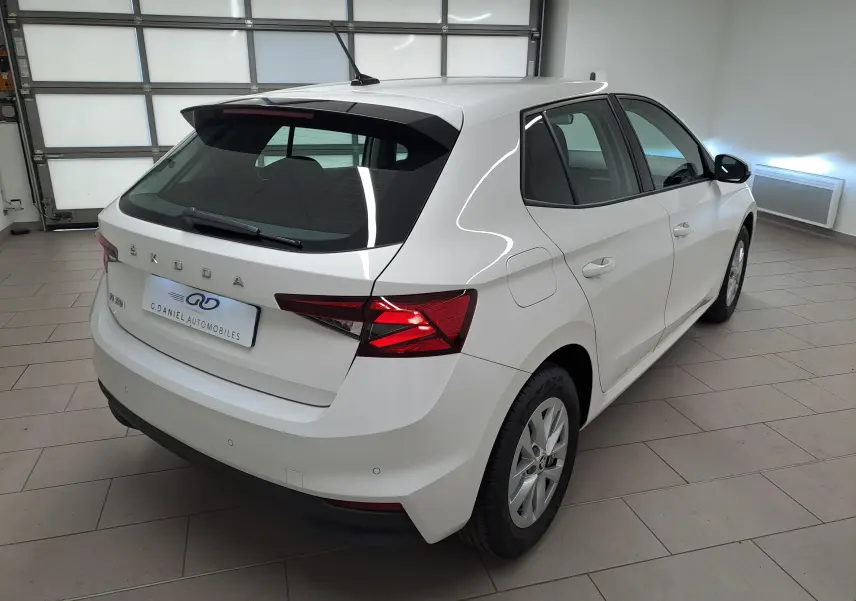 Vue 3/4 arrière droite d'une Skoda Fabia 2023 blanche Candy avec feux arrière allumés dans un garage.