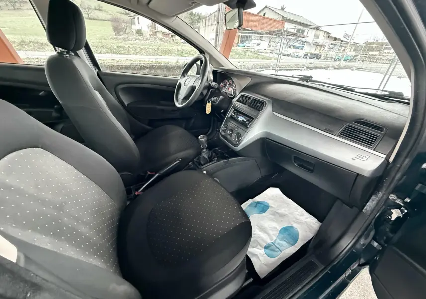 Vue intérieure côté conducteur de la Fiat Punto noire 2009, montrant le tableau de bord et les sièges en tissu noir.