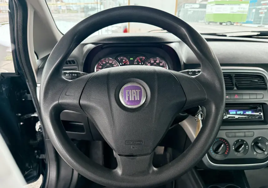 Vue intérieure centrée sur le volant noir de la Fiat Punto 1.2 i 65 de 2009 avec tableau de bord et commandes visibles.