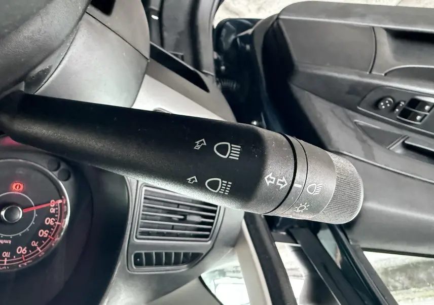 Gros plan sur la commande des phares et clignotants côté gauche dans l’habitacle d’une Fiat Punto noire de 2009.