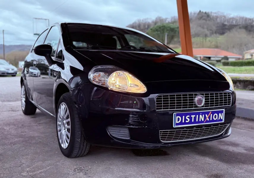 Vue 3/4 avant gauche d'une Fiat Punto noire de 2009 avec phares allumés et plaque "Distinxion" visible.