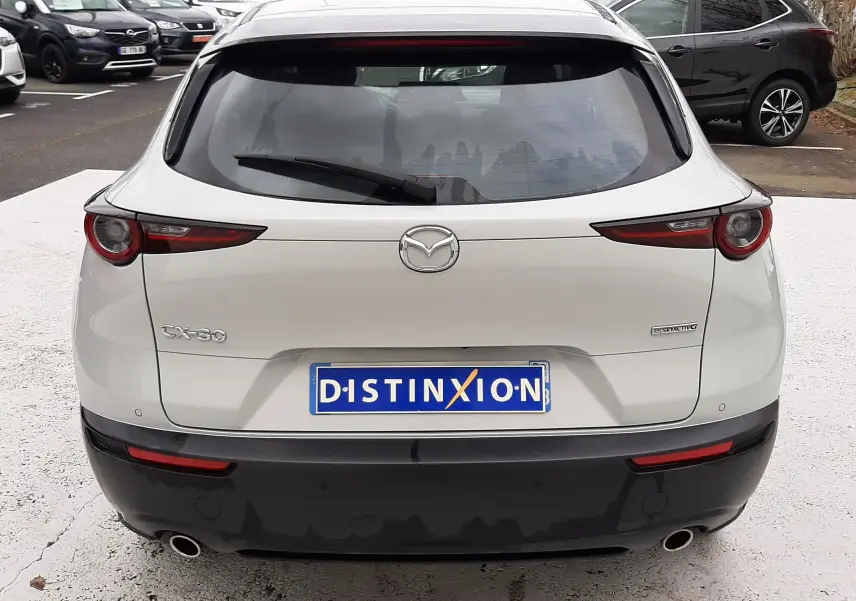 Vue arrière d'un Mazda CX-30 blanc Ceramic White avec feux LED et double sortie d'échappement visible.