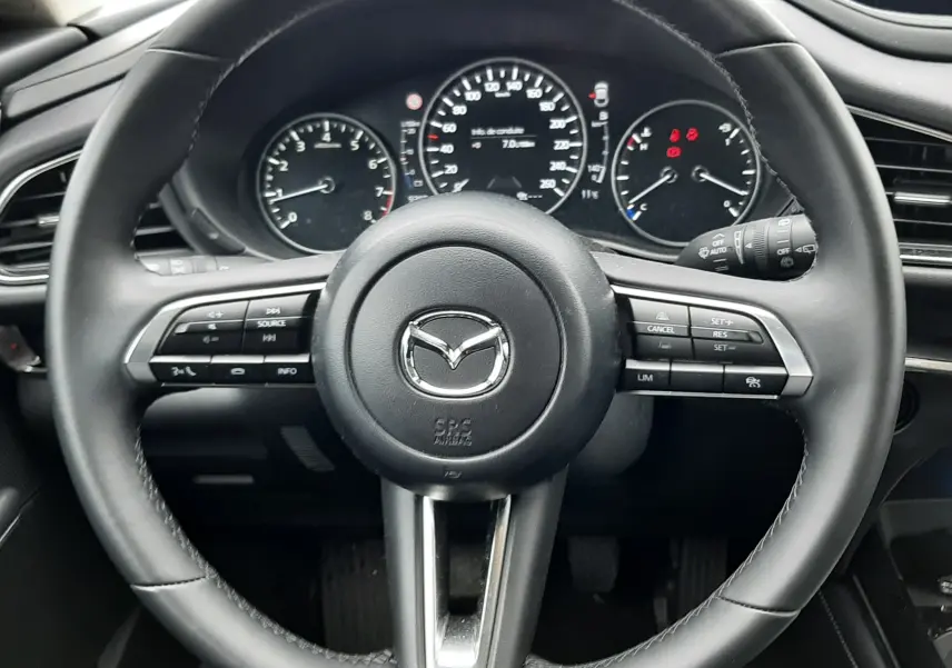 Vue frontale du volant noir de la Mazda CX-30 2024 avec commandes intégrées et tableau de bord digital.