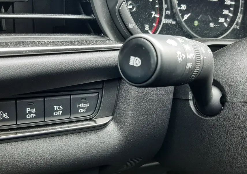 Détail intérieur du tableau de bord côté gauche du Mazda CX-30 2024, montrant commandes et manette de phares.