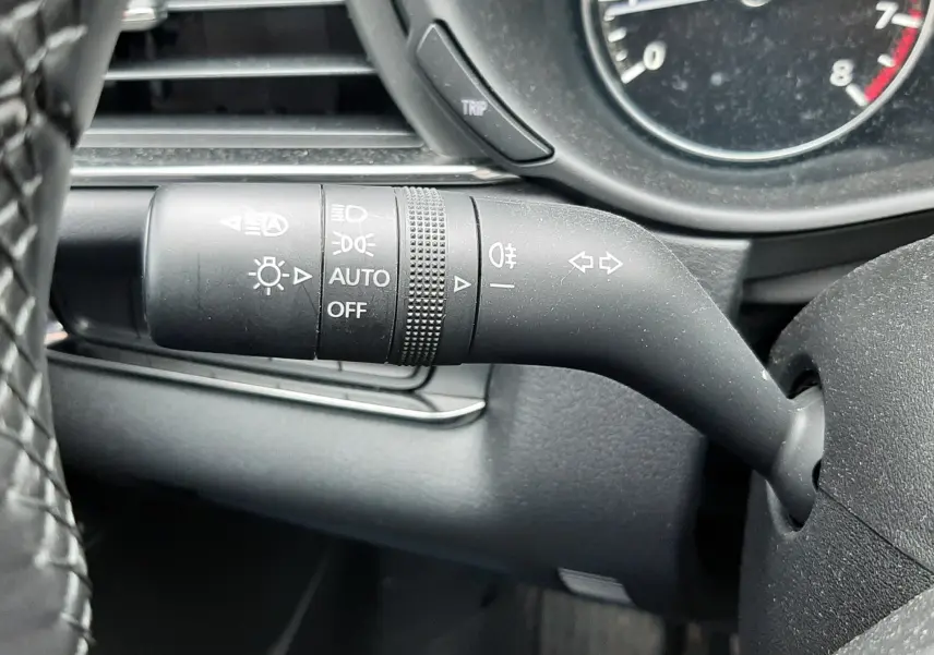 Gros plan sur la manette de clignotants noire à gauche du volant dans l’habitacle noir du Mazda CX-30 2024.