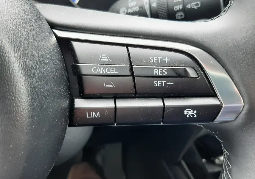 Gros plan sur les commandes de régulateur de vitesse au volant noir du Mazda CX-30 2024, détails des boutons fonctionnels.