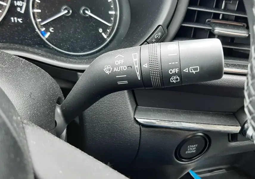 Gros plan sur la commande d'essuie-glace à gauche du volant dans l'habitacle noir du Mazda CX-30 2024.