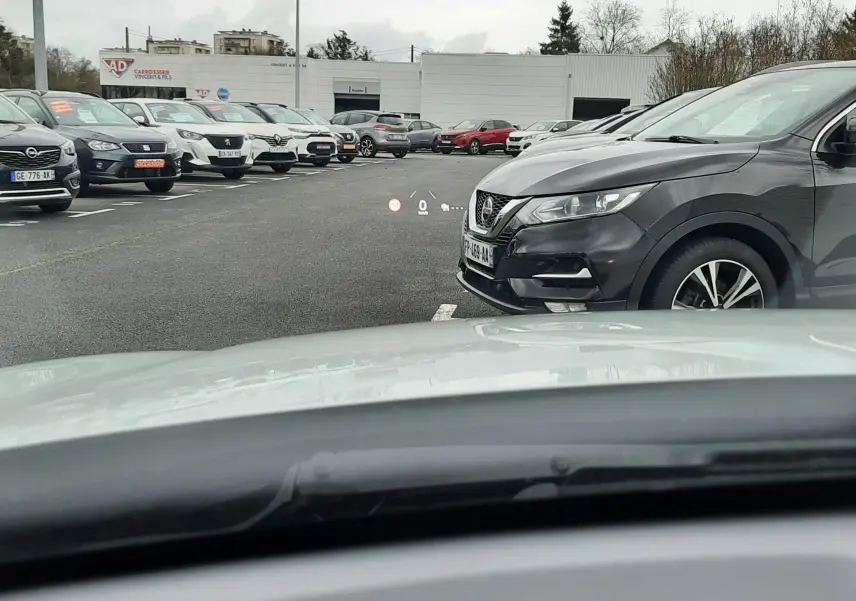 Vue depuis l'habitacle montrant le capot blanc d'une Mazda CX-30 2024 en Ceramic White sur un parking extérieur.