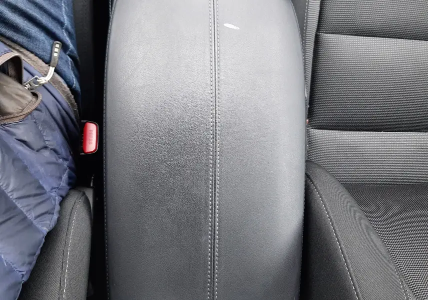 Vue plongeante sur l'accoudoir central en cuir noir du Mazda CX-30 2024, avec coutures apparentes et siège tissu gris.
