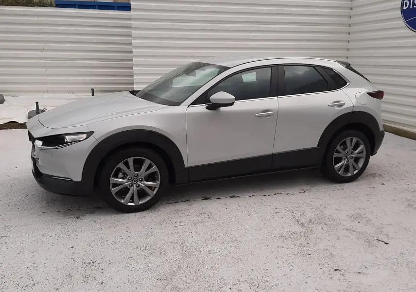 Vue de profil côté gauche d'un Mazda CX-30 2024 blanc céramique avec jantes alliage et protections noires basses.