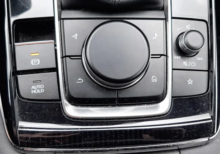 Gros plan sur la molette de commande centrale noire et les boutons environnants du Mazda CX-30 2024 en finition Exclusive Line.