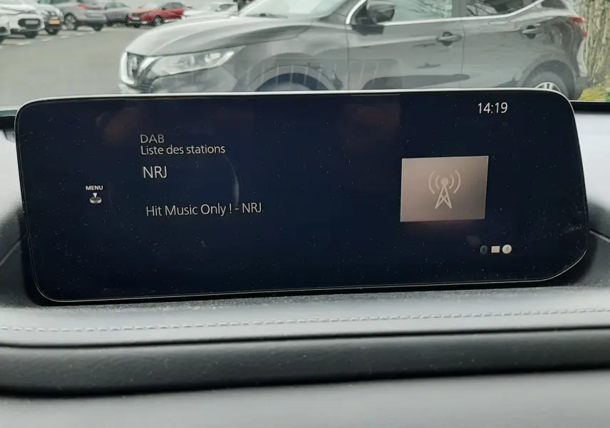Vue intérieure du tableau de bord avec écran multimédia, en arrière-plan un SUV gris foncé en stationnement.