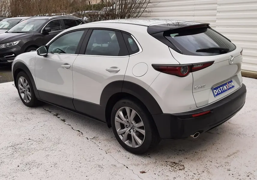 Vue 3/4 arrière droite d'un Mazda CX-30 blanc Ceramic White avec jantes alliage et feux arrière LED distinctifs.