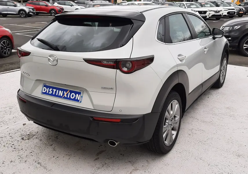 Vue 3/4 arrière droite d'un Mazda CX-30 2024 blanc céramique avec toit noir et feux arrière effilés.