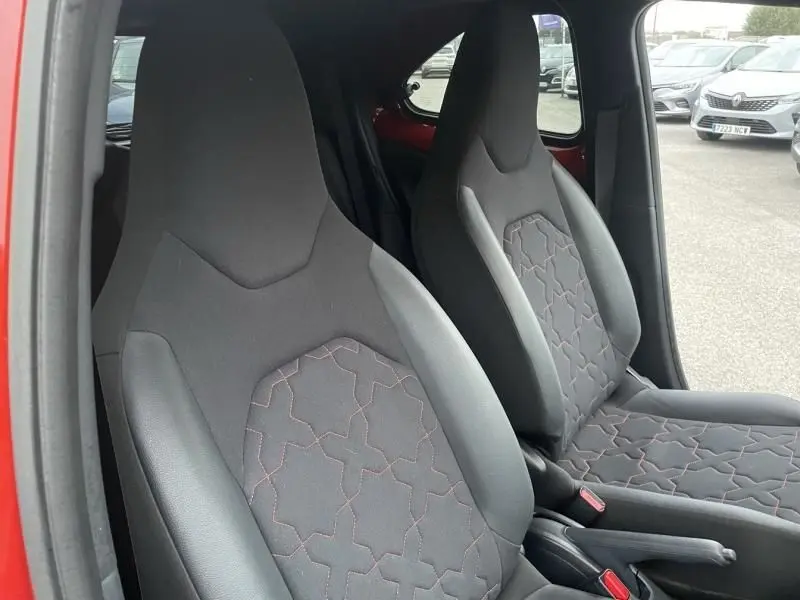 Vue intérieure des sièges avant noirs avec surpiqûres rouges d'une Toyota Aygo X rouge piment au toit noir, côté droit visible.