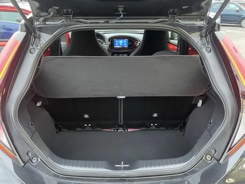Vue arrière du coffre ouvert d'une Toyota Aygo X rouge piment avec toit noir, montrant l'intérieur et le tableau de bord.