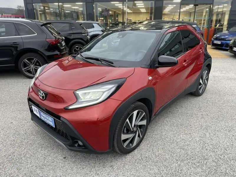Toyota Aygo X rouge piment avec toit noir, vue 3/4 avant droit, détails noirs contrastants et jantes alliage.