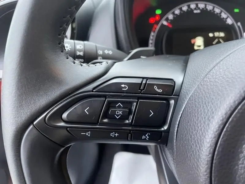 Gros plan sur les commandes au volant côté gauche de la Toyota Aygo X 2023, volant en cuir noir.