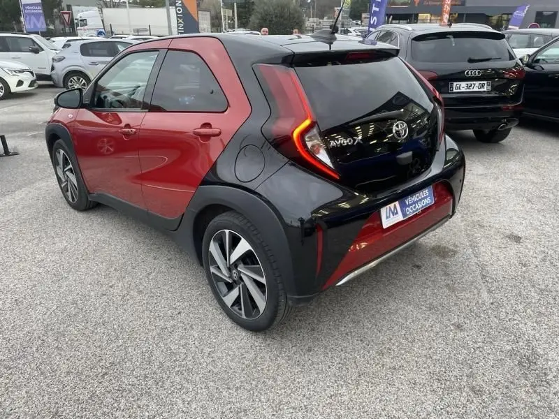 Vue 3/4 arrière droite de la Toyota Aygo X 2023 rouge piment avec toit noir et feux arrière en forme de C.