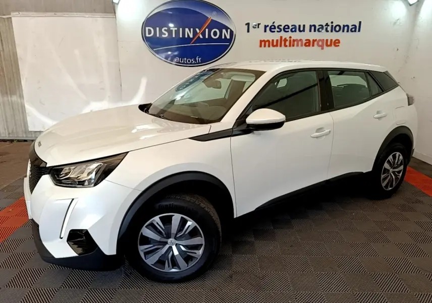 Peugeot 2008 blanc vue 3/4 avant droit, avec phares LED et jantes alliage, sur sol damier intérieur showroom.