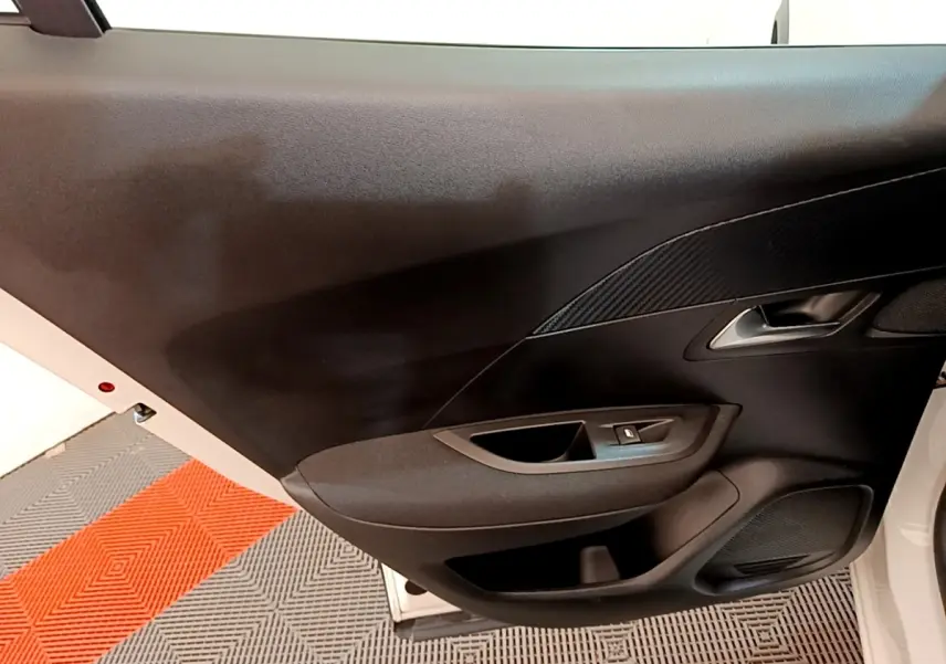 Vue rapprochée de la porte avant gauche noire d’un Peugeot 2008 blanc, avec poignée et commande de lève-vitre.