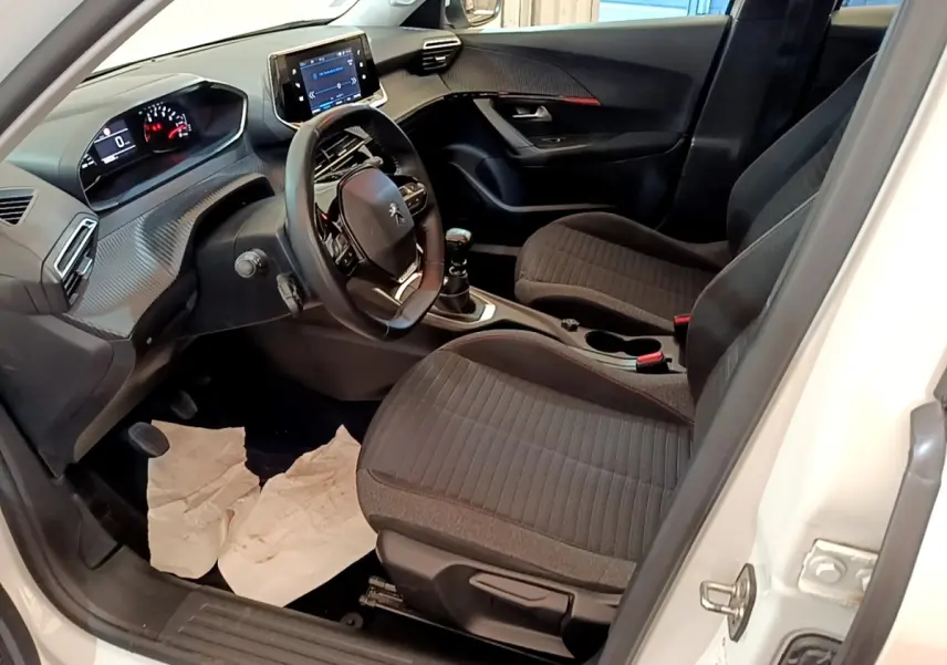 Vue intérieure côté conducteur du Peugeot 2008 blanc, montrant le volant cuir, tableau de bord et écran tactile central.