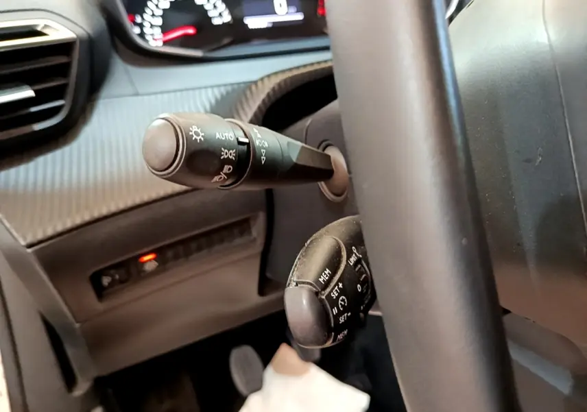 Gros plan sur la commande des phares et du régulateur de vitesse derrière le volant d’un Peugeot 2008 blanc.
