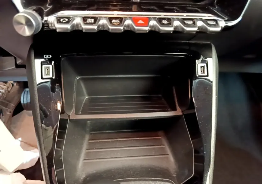 Gros plan sur la console centrale noire de la Peugeot 2008 blanche, avec boutons de commande et ports USB visibles.