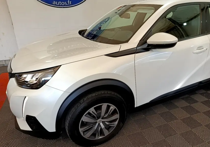 Vue 3/4 avant droit d'un Peugeot 2008 blanc avec jantes alliage et rétroviseur blanc sur fond intérieur.