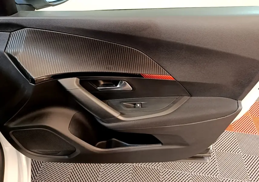 Vue intérieure côté gauche de la porte d’une Peugeot 2008 blanche avec insert décor carbone et bouton de lève-vitre.