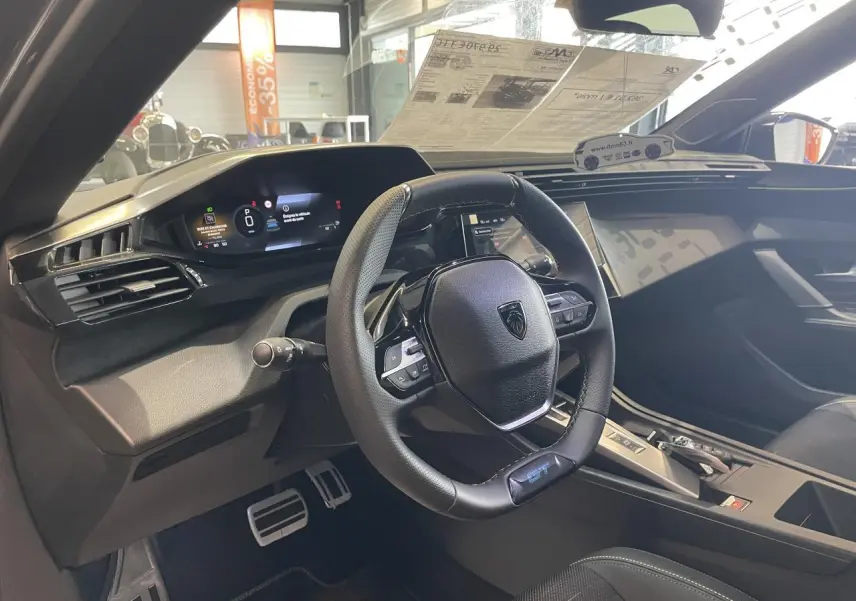 Vue intérieure du poste de conduite de la Peugeot 308 GT 2026, volant cuir GT avec surpiqûres vert Adamite et tableau de bord numérique.