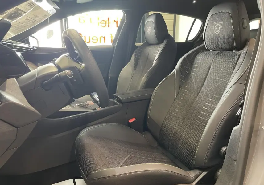 Vue intérieure côté conducteur de la Peugeot 308 gris selenium, sièges noirs avec logo Peugeot brodé sur appuie-tête.