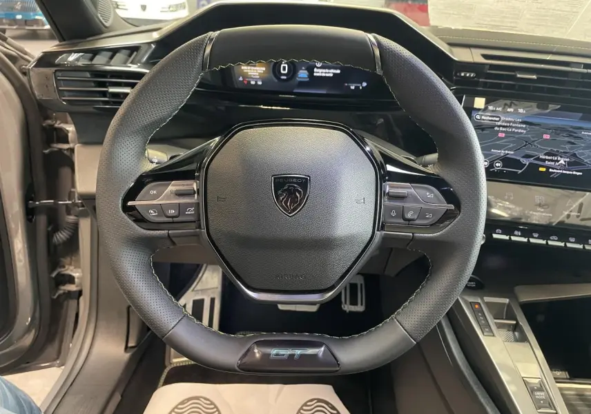 Volant compact GT en cuir noir avec logo Peugeot, vue de face sur tableau de bord numérique et console centrale.