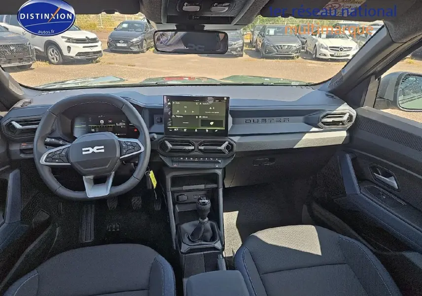Vue intérieure avant du Dacia Duster 2025, tableau de bord gris avec écran tactile et volant multifonction noir.