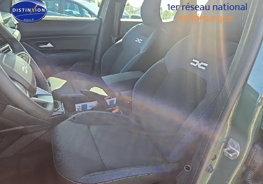 Vue intérieure côté conducteur du Dacia Duster vert kaki 2025, sièges tissu avec logo DC brodé et accoudoir central.