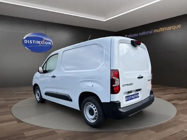 Vue 3/4 arrière droite d'un utilitaire Citroën Berlingo blanc avec protections noires et jantes acier en showroom.