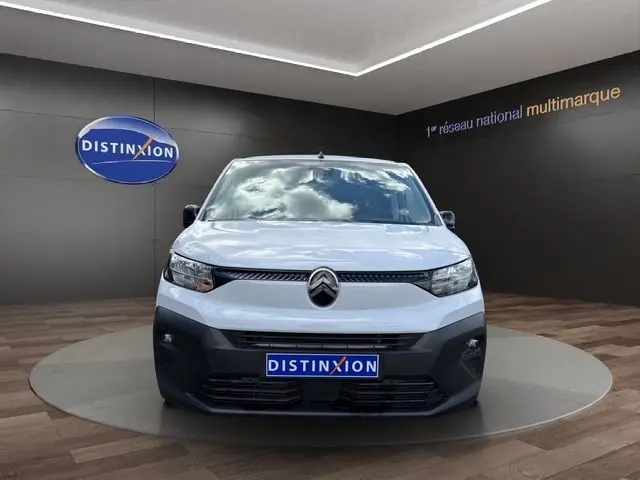 Vue de face d'un Citroën Berlingo blanc 2025 avec calandre noire et logo central, sur fond intérieur showroom.