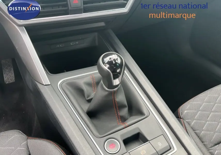 Gros plan sur la console centrale et levier de vitesses manuel du SEAT LEON ST gris métallique, intérieur tissu noir avec surpiqûres rouges.