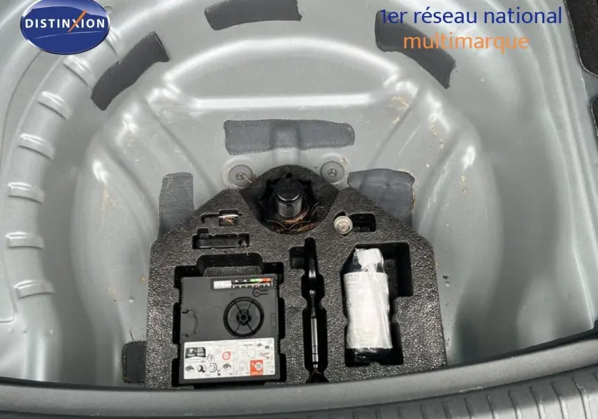 Vue plongeante sur le coffre ouvert d'une SEAT LEON ST gris magnétique, montrant le rangement pour roue de secours et outils.