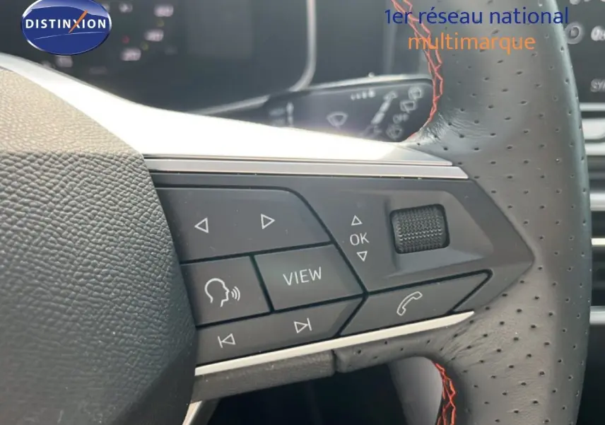 Gros plan sur les commandes multifonctions à droite du volant perforé avec surpiqûres rouges du SEAT LEON ST gris magnétique.