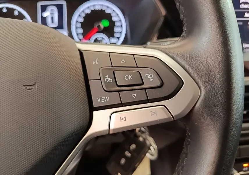 Gros plan sur le volant cuir noir du Volkswagen T-Cross 2022, avec commandes multifonctions et tableau de bord partiellement visible.